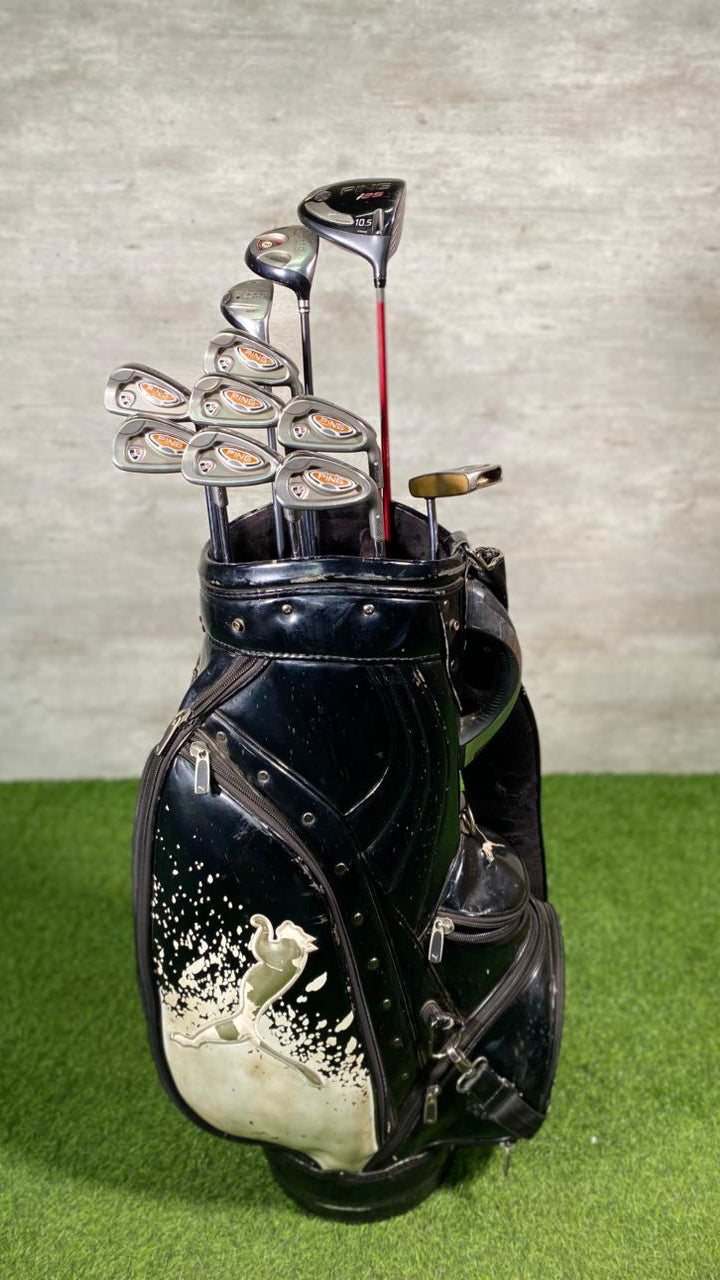 Black golf bag with golf clubs on a green surface and gray background