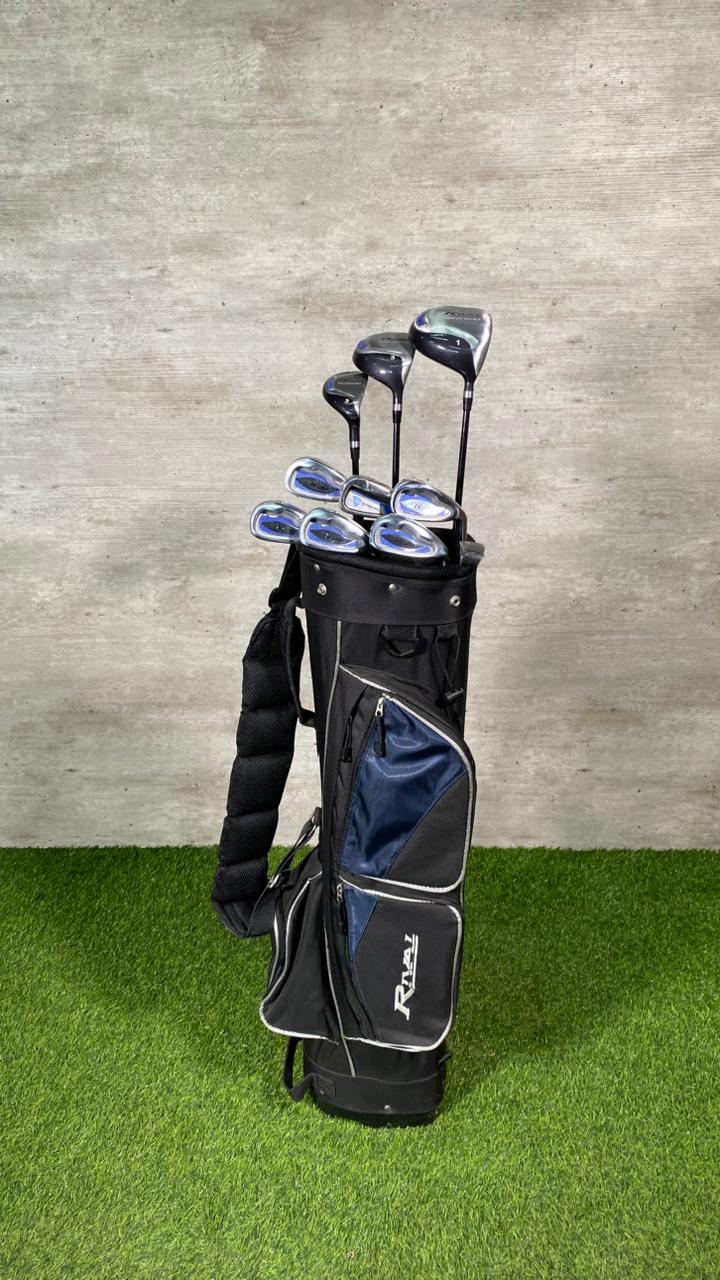 Set of golf clubs in a black and gray bag on green grass with a concrete wall background