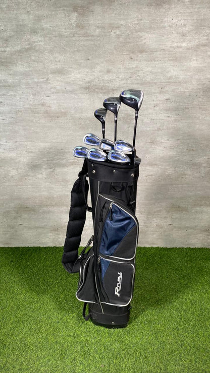 Set of golf clubs in a black and gray bag on green grass with a concrete wall background