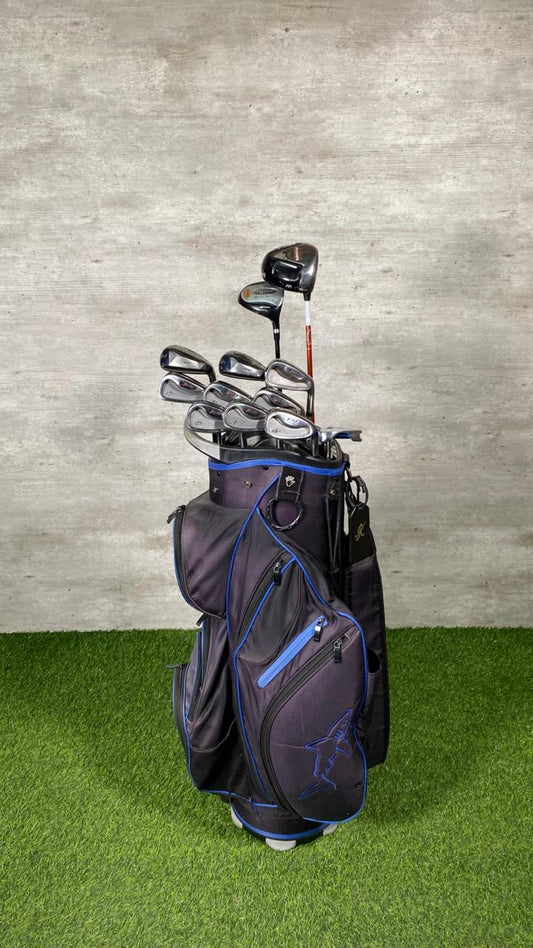 Golf bag with clubs on a grassy surface against a concrete wall