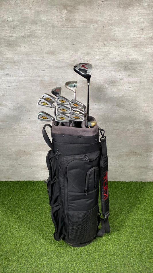 Set of golf clubs in a black bag on green grass with a gray concrete wall background