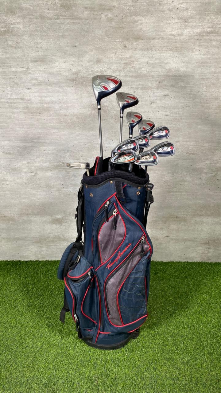 Golf clubs in a blue bag on grass with a gray wall background