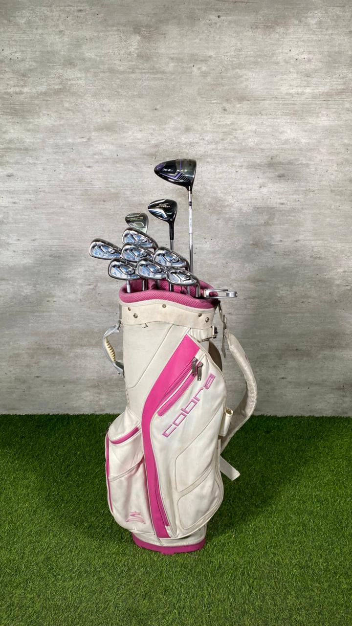 Golf club set in a white and pink bag on a green surface with a gray background