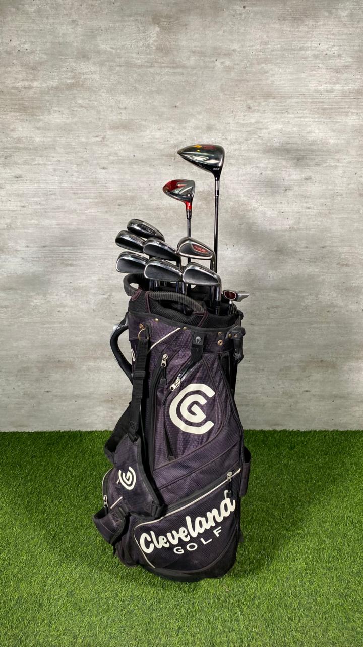 Golf clubs in a Cleveland Golf bag on a grassy surface with a concrete wall background