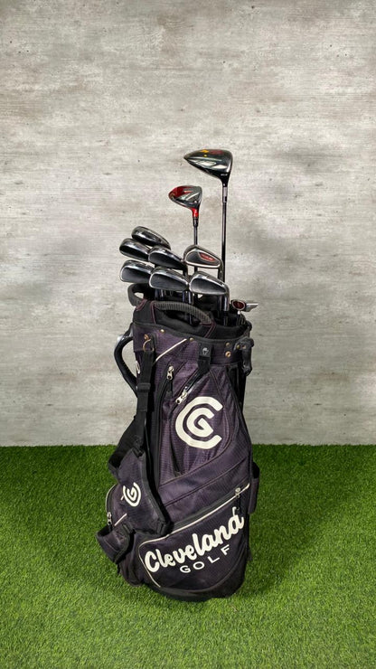 Golf clubs in a Cleveland Golf bag on a grassy surface with a concrete wall background
