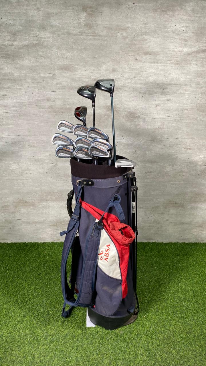 Golf bag with clubs on a grassy surface against a concrete wall