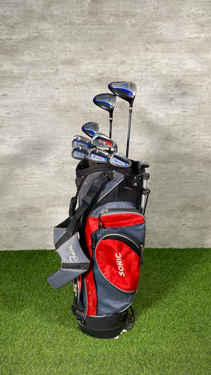 Golf bag with clubs on a grassy surface against a concrete wall