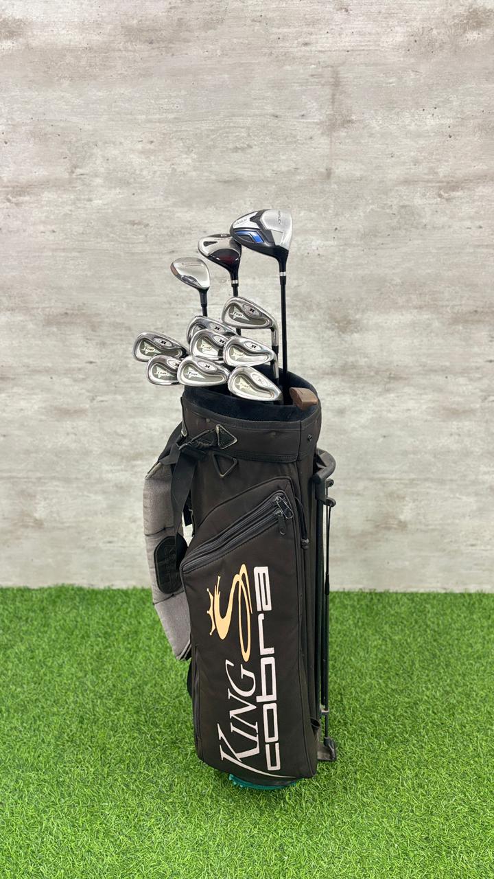 Golf clubs in a black bag on green grass with a gray concrete wall background