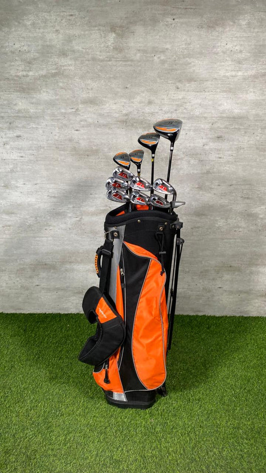 Golf clubs in an orange and black bag on a green grass surface with a gray concrete wall background