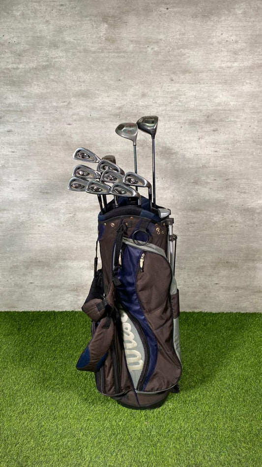Golf bag with clubs on a grassy surface against a concrete wall