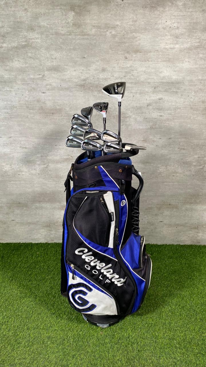Golf bag with golf clubs on a grassy surface against a gray wall