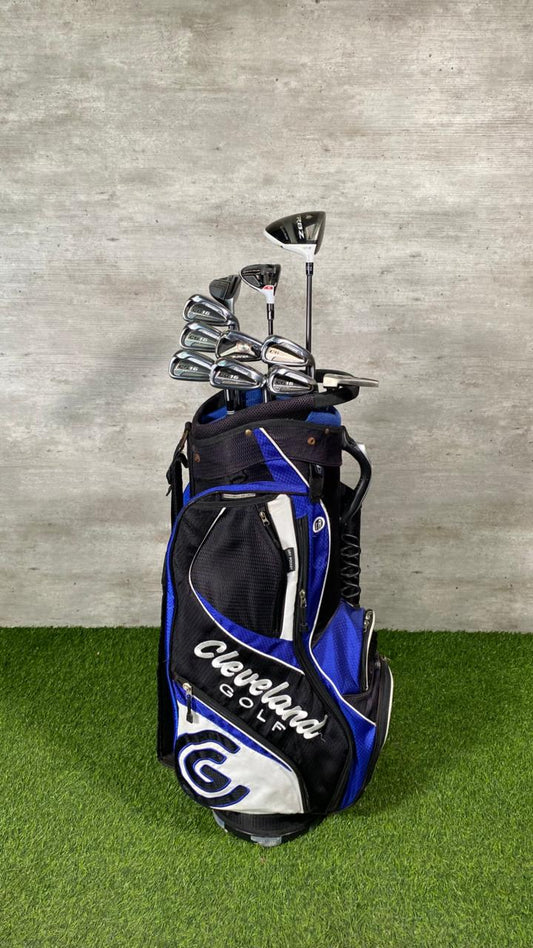 Golf bag with golf clubs on a grassy surface against a gray wall