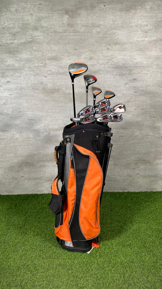 Golf clubs in an orange and black bag on a grassy surface with a gray wall background