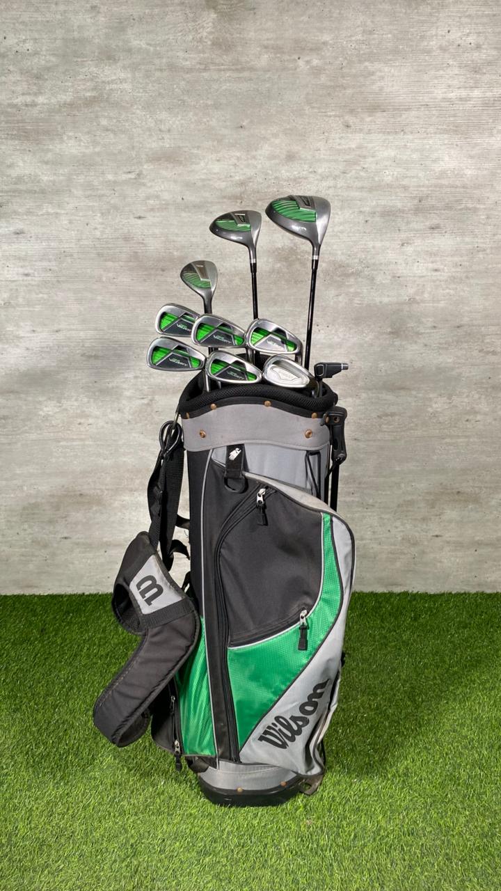 Golf clubs in a bag on grass with a gray wall background