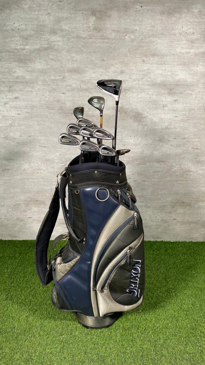 Golf bag with clubs on a grassy surface against a concrete wall