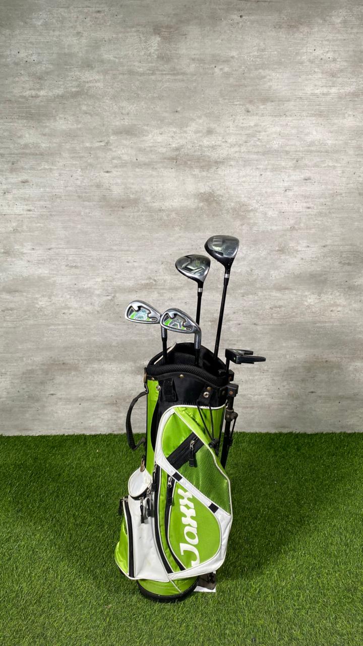Golf clubs in a green and white bag on a grassy surface with a concrete wall background