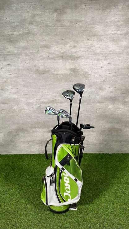 Golf clubs in a green and white bag on a grassy surface with a concrete wall background