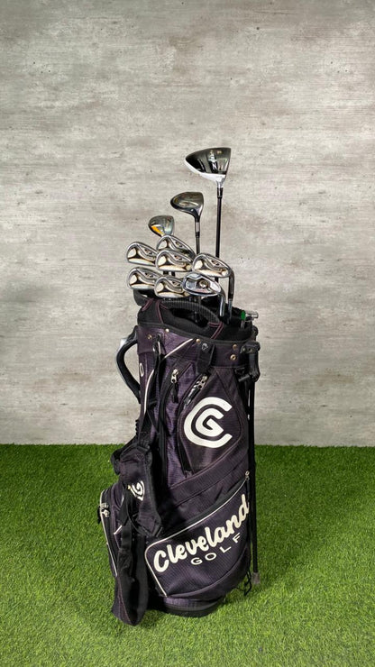 Golf clubs in a Cleveland Golf bag on a grassy surface with a concrete wall background