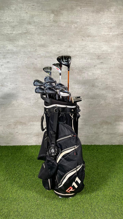 Golf clubs in a black bag on a green grass surface with a gray concrete wall background