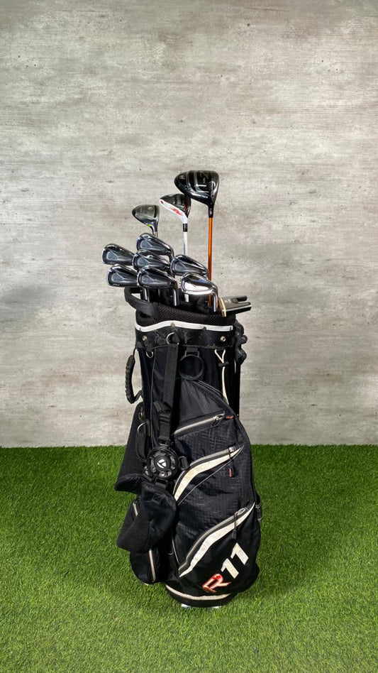 Golf clubs in a black bag on a green grass surface with a gray concrete wall background