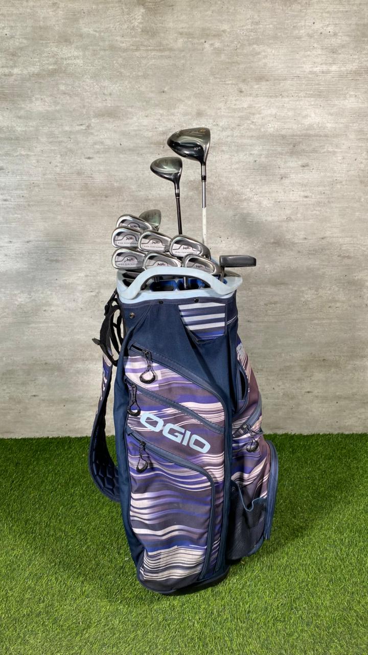 Golf bag with golf clubs on a grassy surface against a concrete wall.