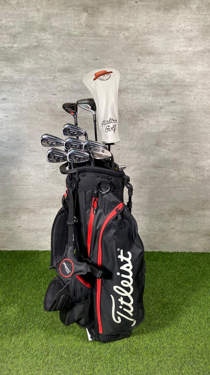 Golf clubs in a Titleist bag on grass with a gray wall background