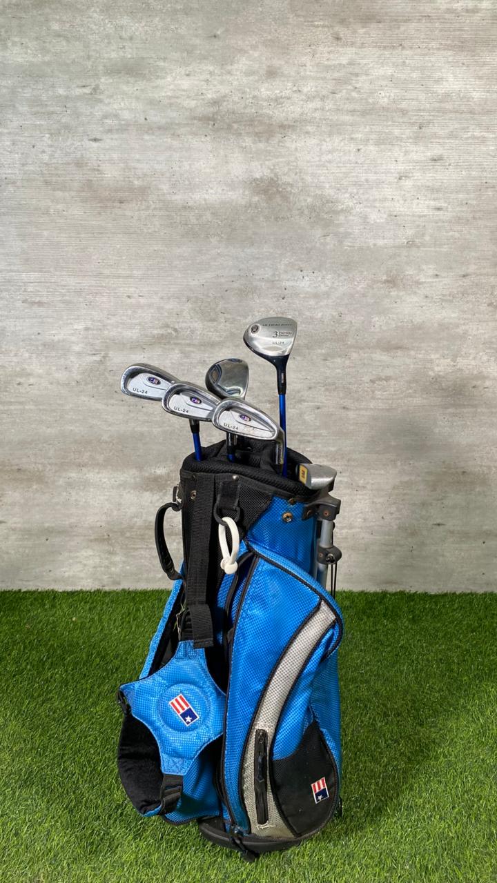 Blue golf bag with golf clubs on a grassy surface against a concrete wall.