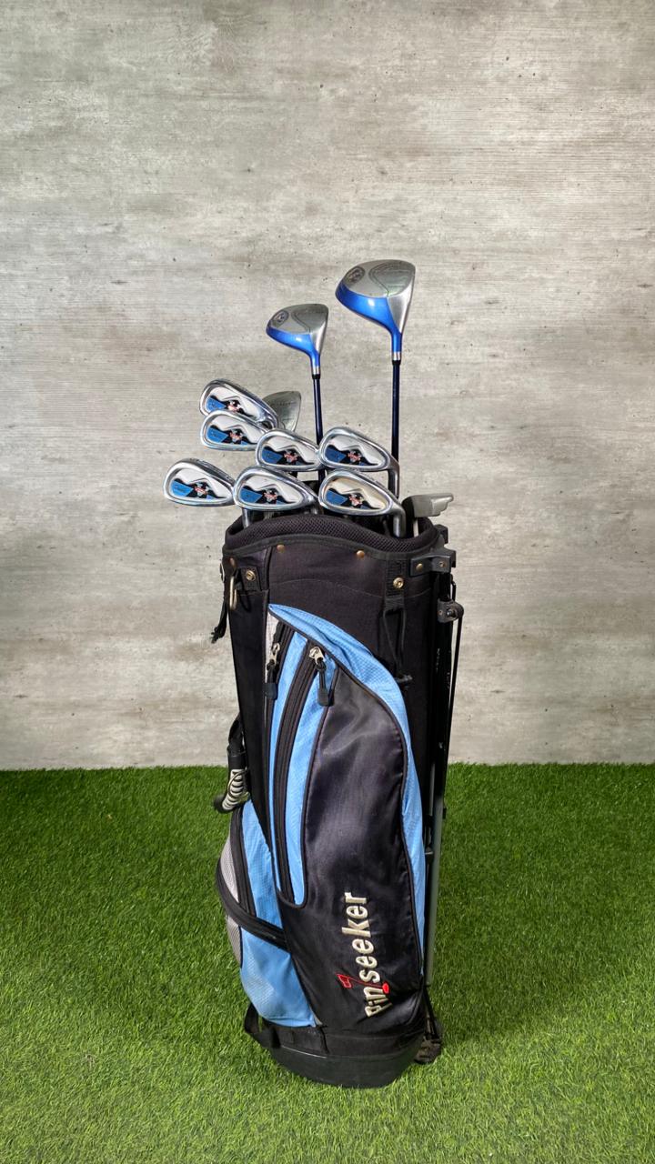 Golf clubs in a black and blue bag on a grassy surface with a gray concrete wall background