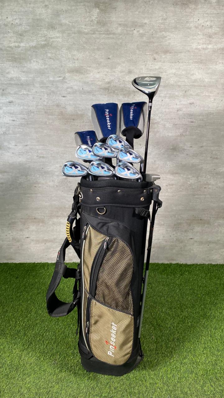 Golf club set with clubs and balls in a bag on grass against a concrete wall.
