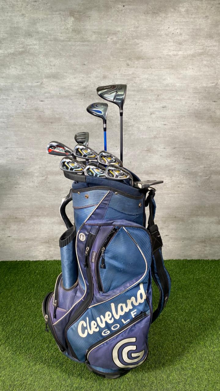 Golf bag with clubs on a grassy surface against a concrete wall
