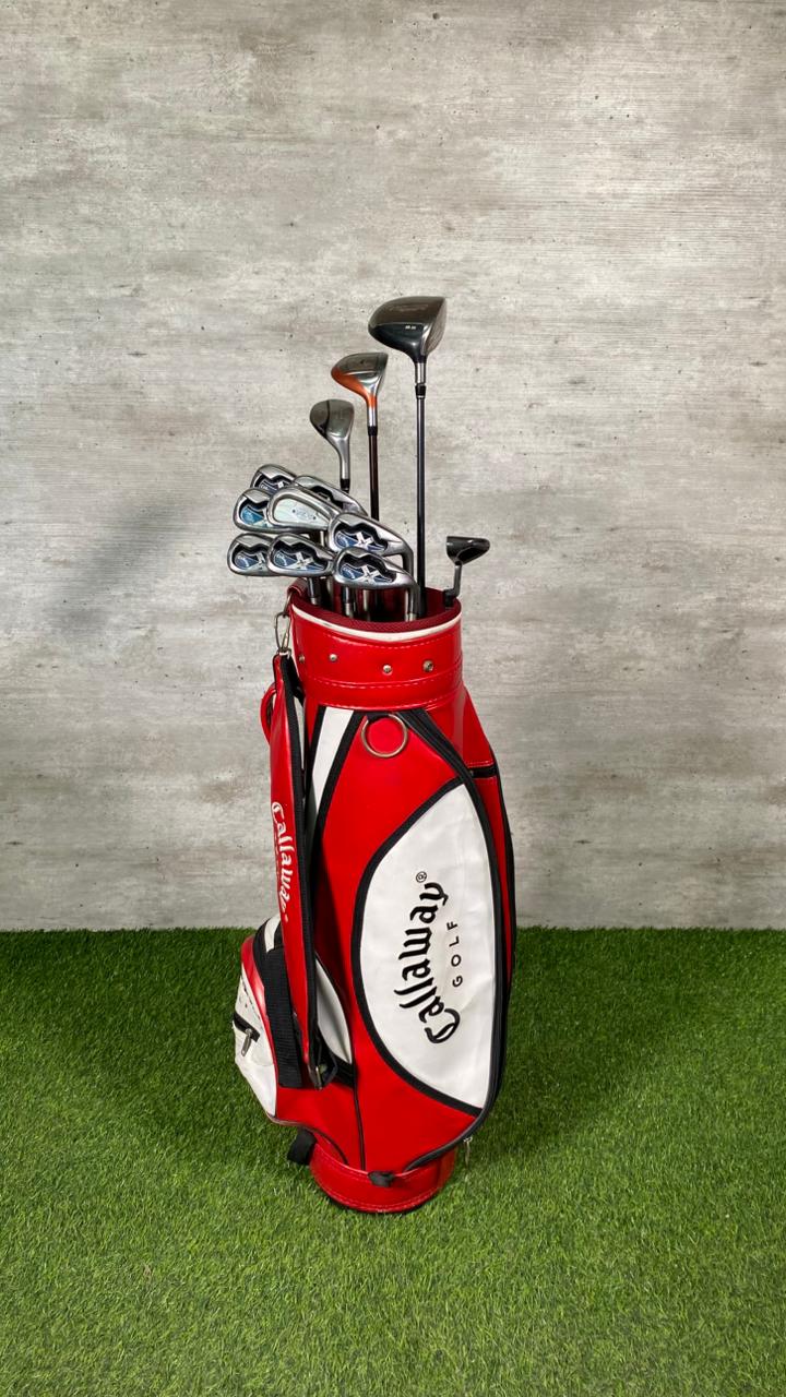 Red and white Callaway golf bag with golf clubs on a grassy surface and concrete wall background