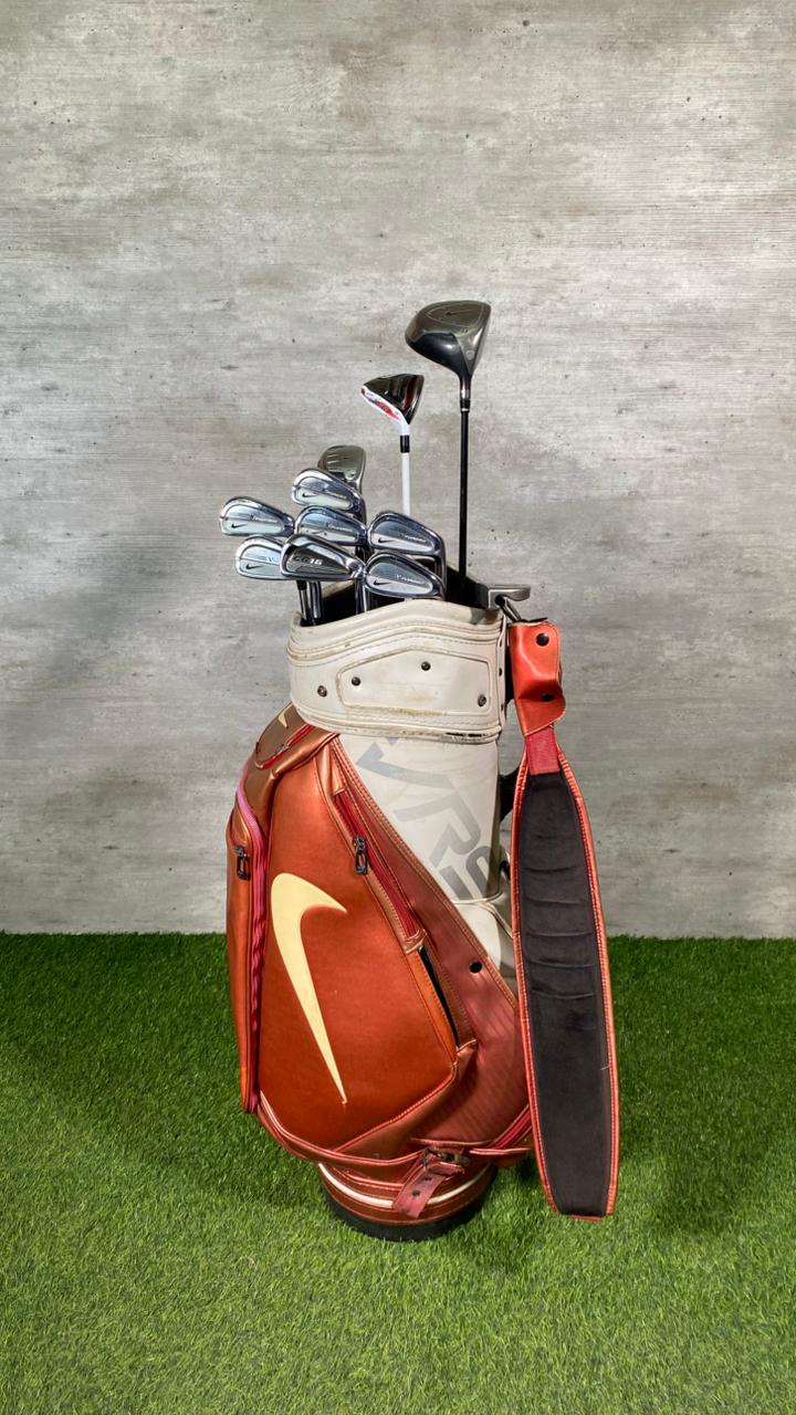 Golf clubs in a red and white bag on a grassy surface with a concrete wall background