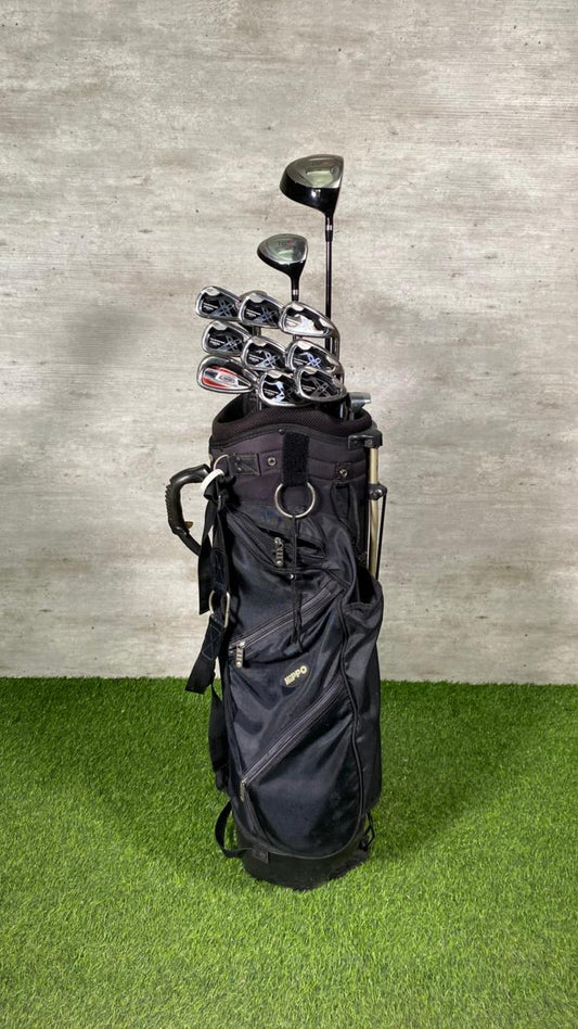 Black golf bag with golf clubs on a green grass and gray concrete background