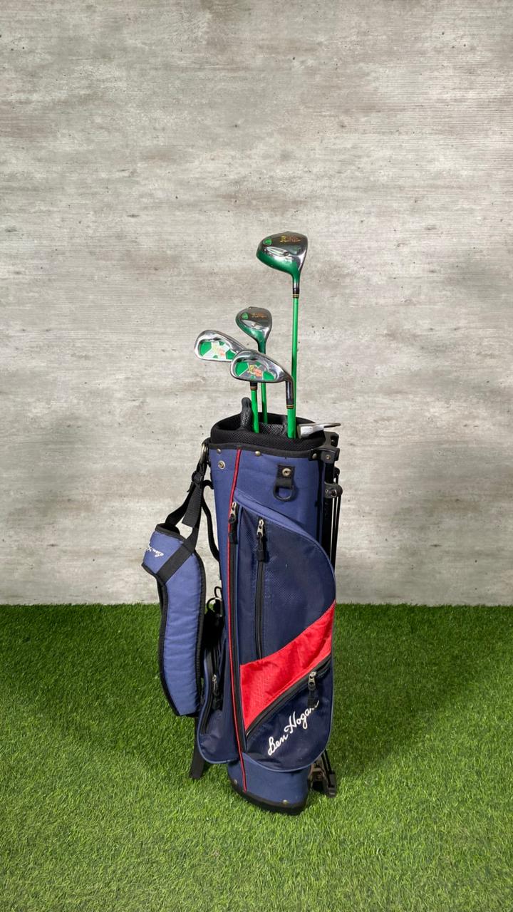 Golf bag with golf clubs on a grassy surface against a concrete wall.