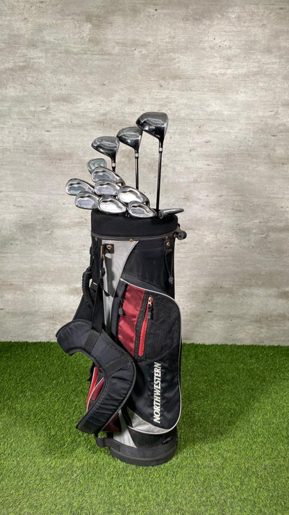 Set of golf clubs in a black bag on a grassy surface with a concrete wall background