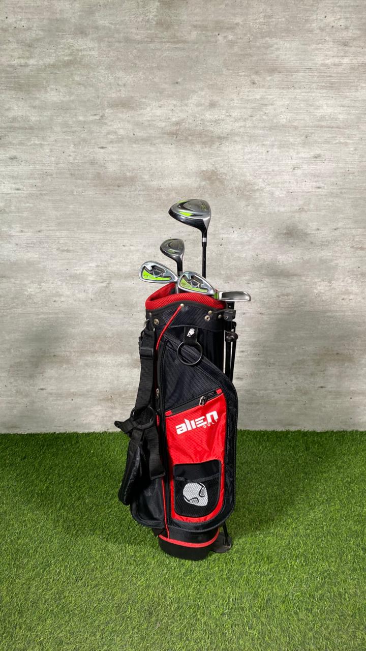 Golf clubs in a red and black bag on a grassy surface with a concrete wall background