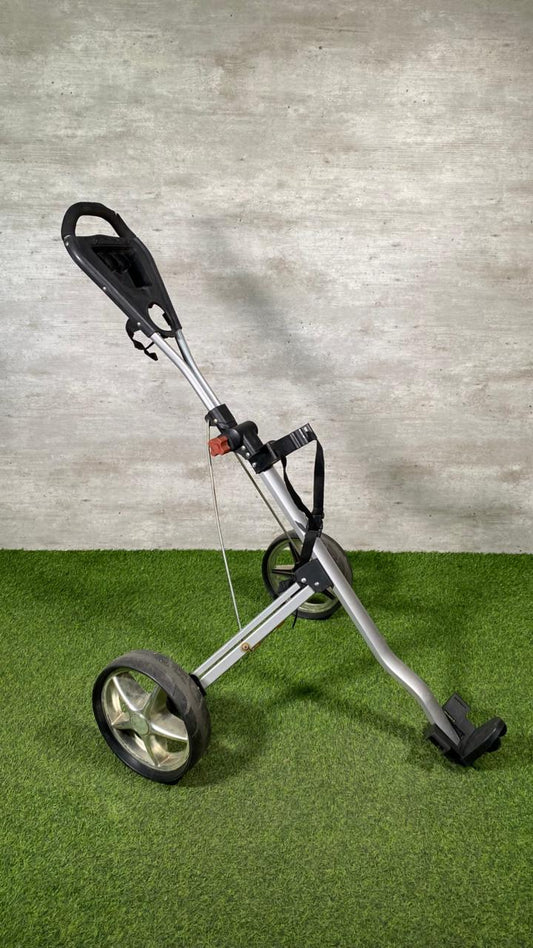 Golf push cart on a green surface with a gray concrete wall background