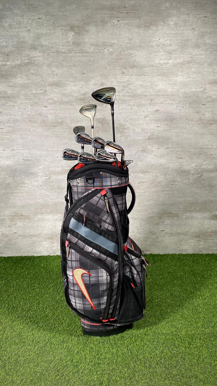 Golf bag with golf clubs on a grassy surface with a concrete wall background
