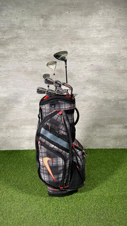 Golf bag with golf clubs on a grassy surface with a concrete wall background