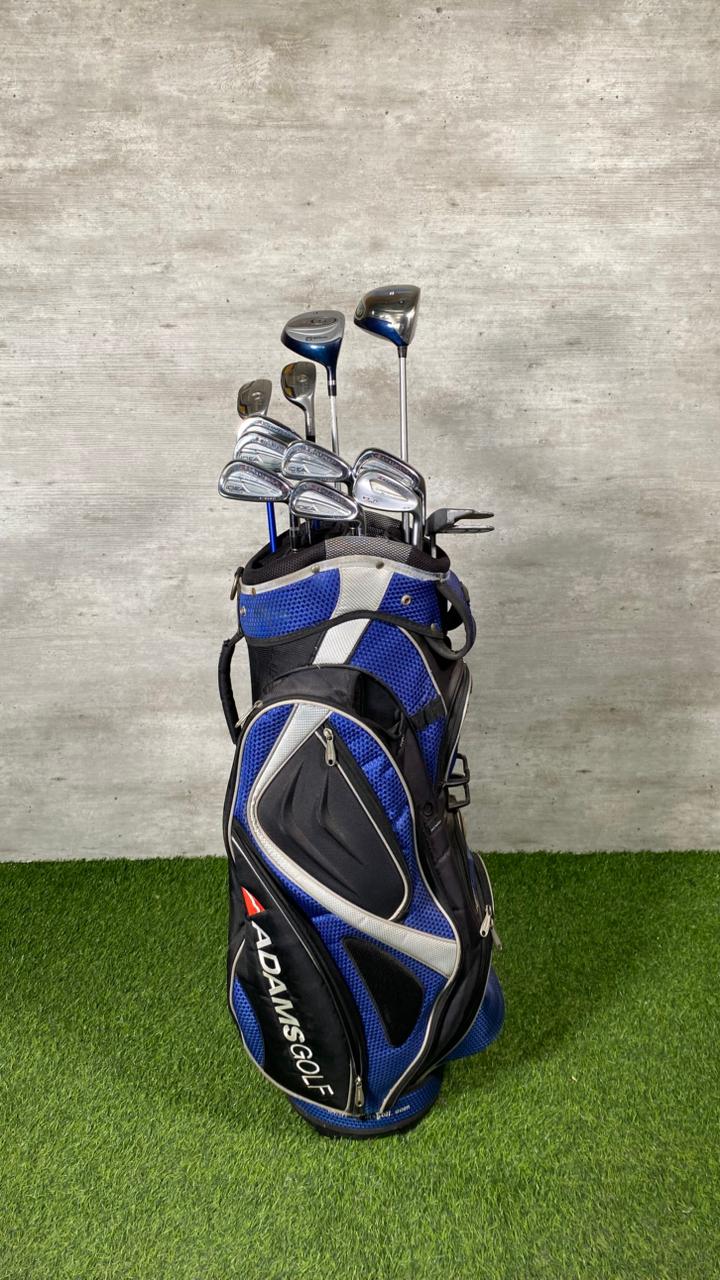 Golf club set in a blue and black bag on grass with a gray wall background