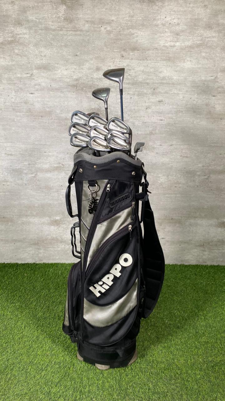 Golf bag with clubs on a grassy surface against a textured wall