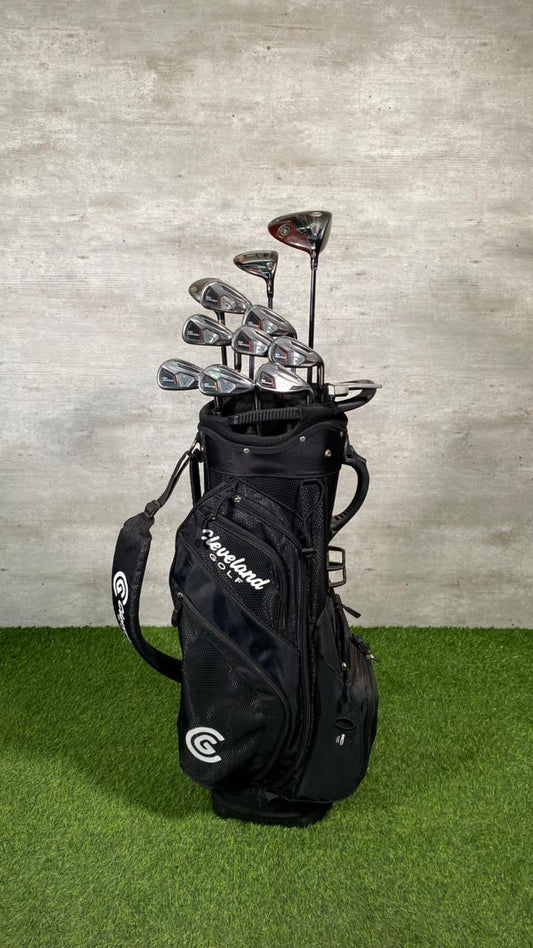 Golf club set in a black bag on a grassy surface with a gray concrete wall background