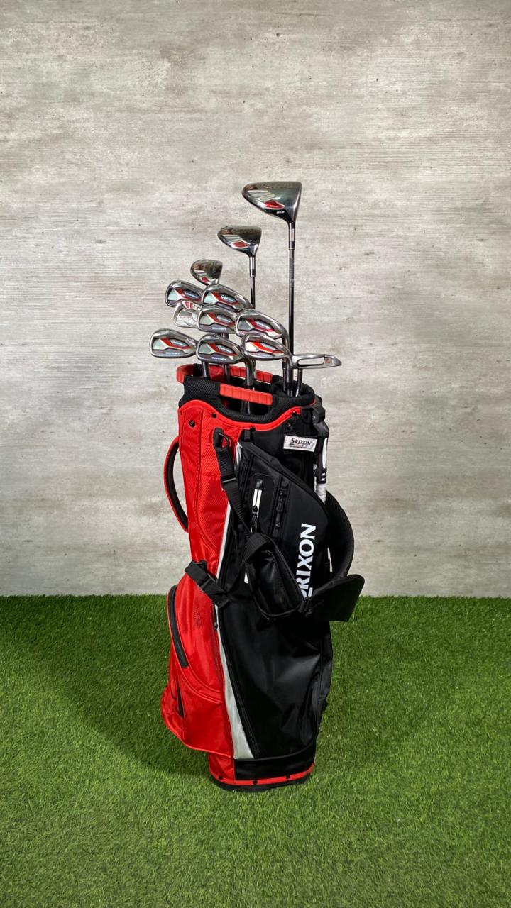 Golf clubs in a red and black bag on a grassy surface with a concrete wall background