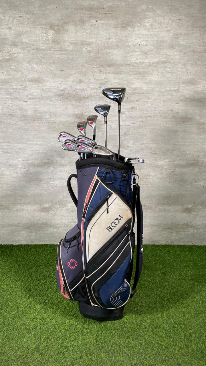 Golf bag with clubs on a grassy surface against a concrete wall