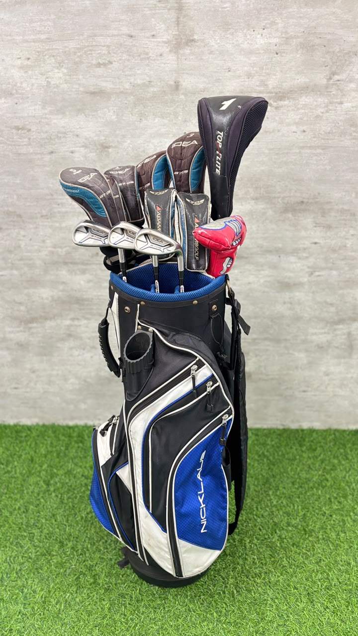 Golf clubs in a blue and black bag on a green surface with a gray wall background