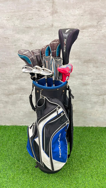 Golf clubs in a blue and black bag on a green surface with a gray wall background