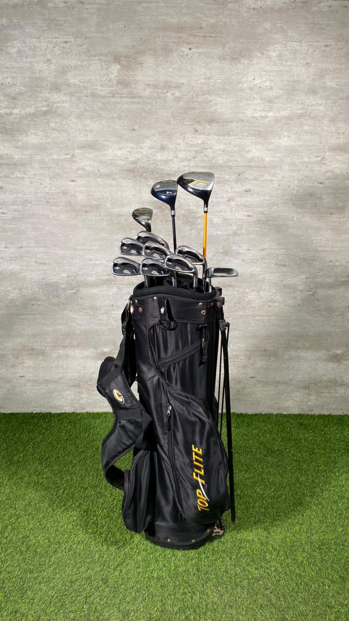Set of golf clubs in a black bag on a grassy surface with a gray concrete wall background