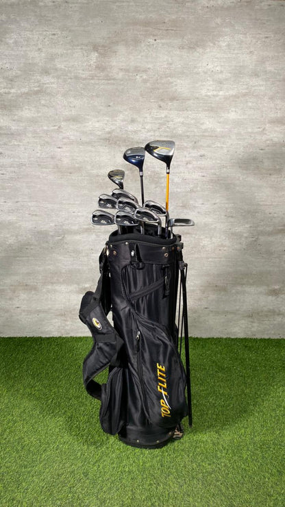 Set of golf clubs in a black bag on a grassy surface with a gray concrete wall background