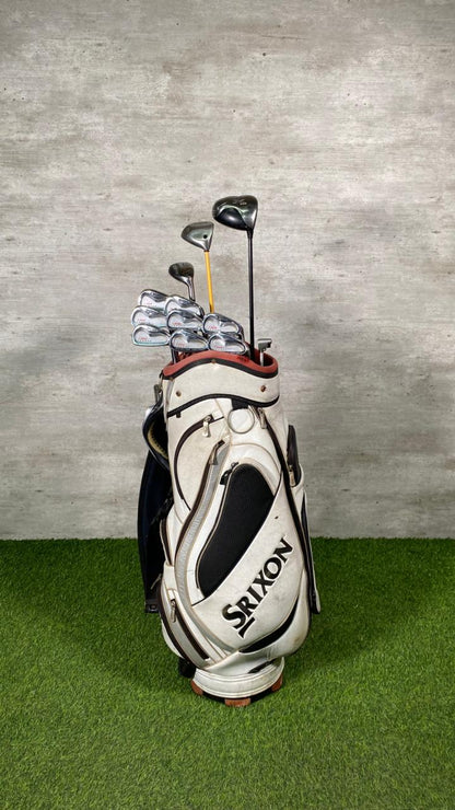 Golf bag with clubs on a grassy area against a gray wall