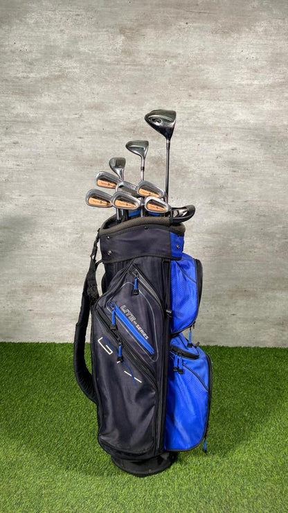 Golf clubs in a black and blue bag on grass with a gray wall background